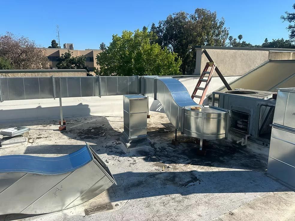 Rooftop with HVAC units, silver ductwork, and a ladder under a clear blue sky
