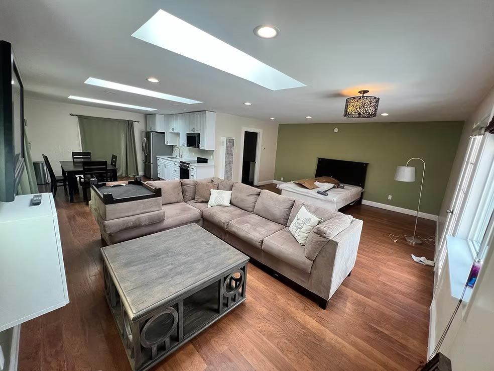 Bright living room with gray sectional sofa, coffee table, TV, hardwood floors, and skylights