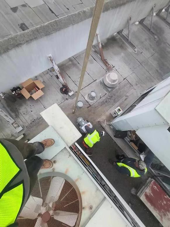 Workers in neon safety vests stand on a rooftop beside HVAC units and building ledges.