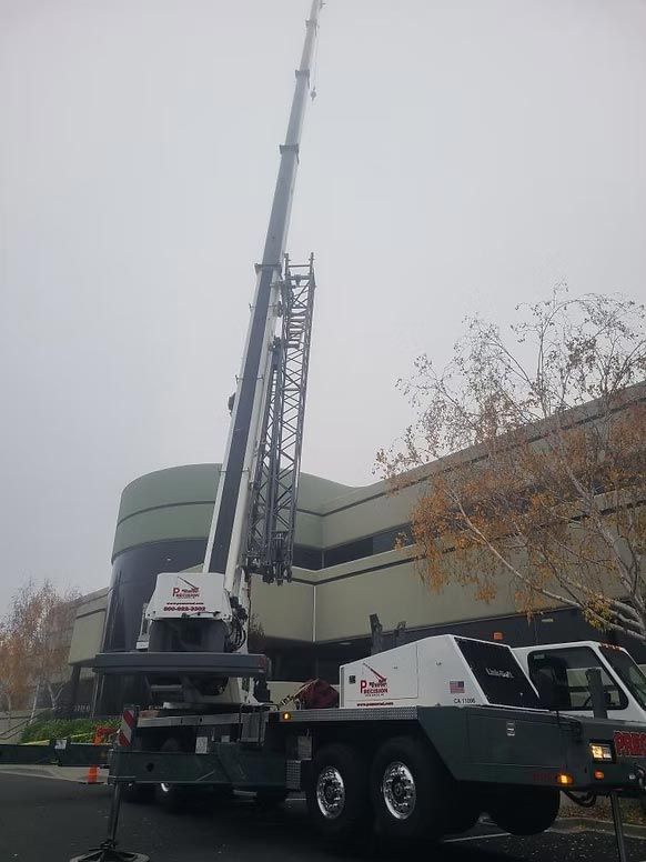 Large crane truck with extended boom parked beside a building under an overcast sky