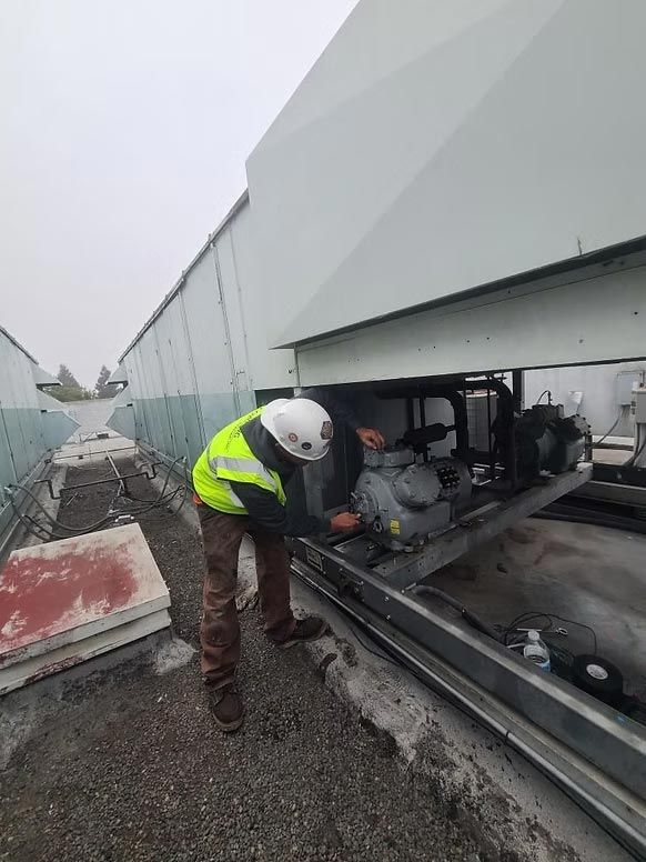 Worker in a high-visibility jacket inspecting machinery beside a white industrial wall outdoors