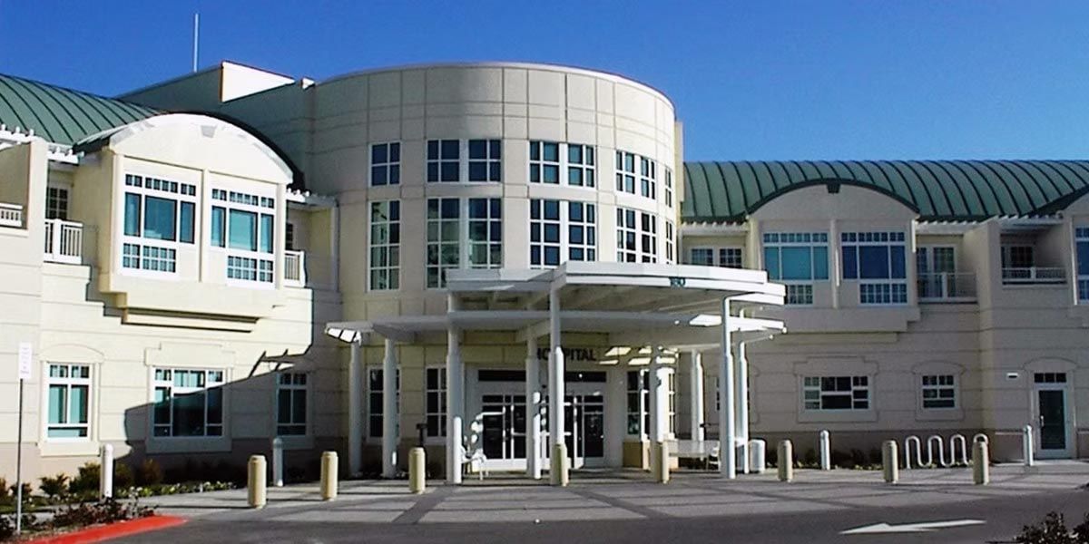 Modern white civic building with large central glass entrance and columns under a blue sky