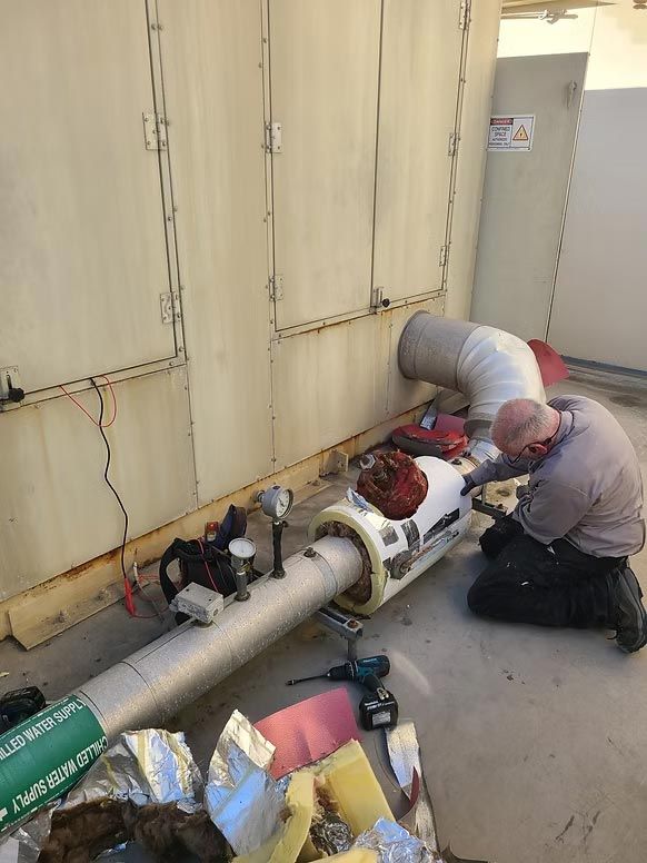 Technicians repairing a large industrial pipe beside a wall in a utility room