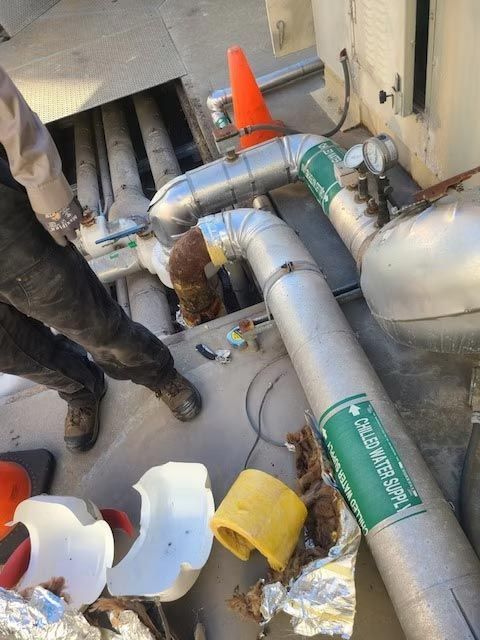 Workers inspecting silver ducting with orange cone and tools on a rooftop HVAC system