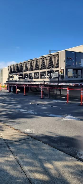 Large industrial cooling unit on red supports beside a paved lot under a clear blue sky