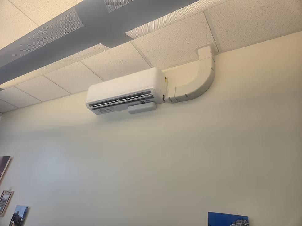 Ceiling-mounted air conditioner with a white duct against a light-colored wall in an indoor room