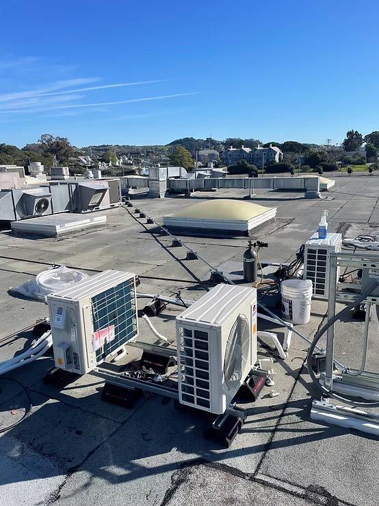 Rooftop with multiple HVAC units and ductwork under a clear blue sky