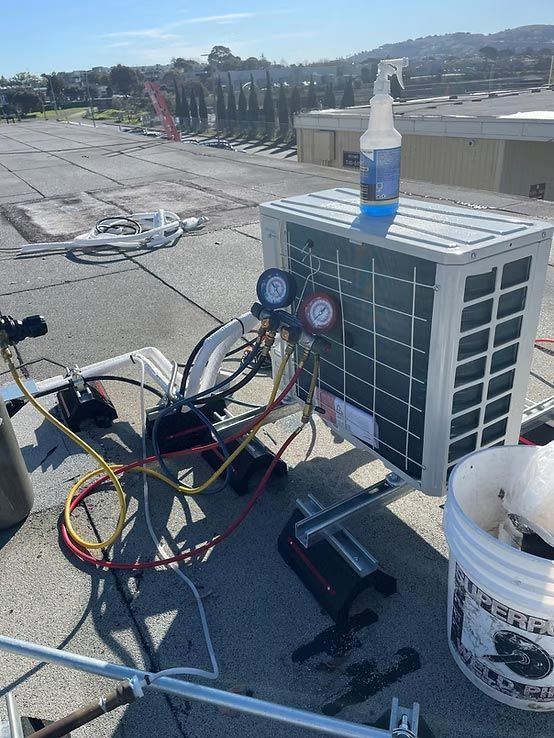 Outdoor HVAC unit with gauges, hoses, and cleaning spray bottle on a rooftop or parking lot surface