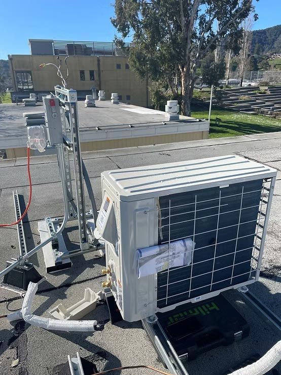 White rooftop HVAC unit with exposed piping and wires on a building roof in sunlight