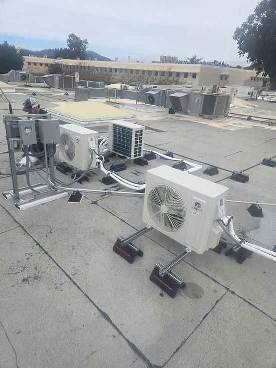 Rooftop with several air conditioning units and HVAC equipment on a flat gray roof under cloudy skies