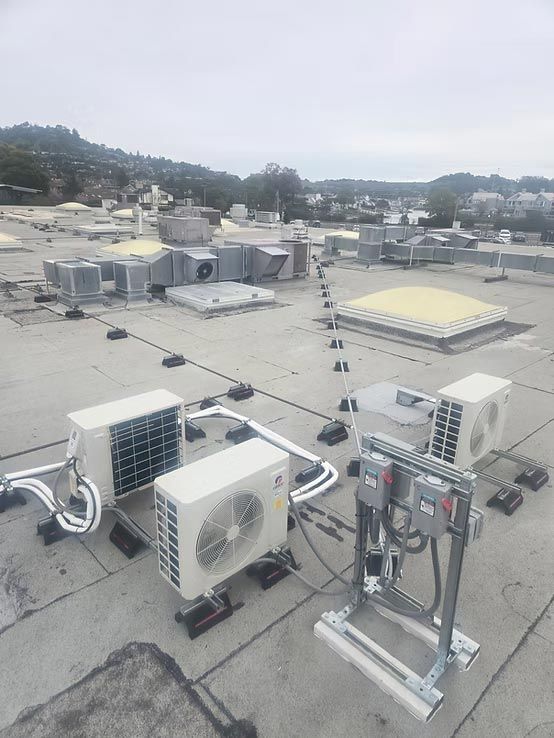 Rooftop HVAC units and vents on a flat commercial roof with hills in the background.
