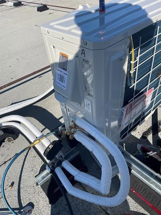White rooftop HVAC unit with insulated hoses and wiring on a flat roof under bright sunlight