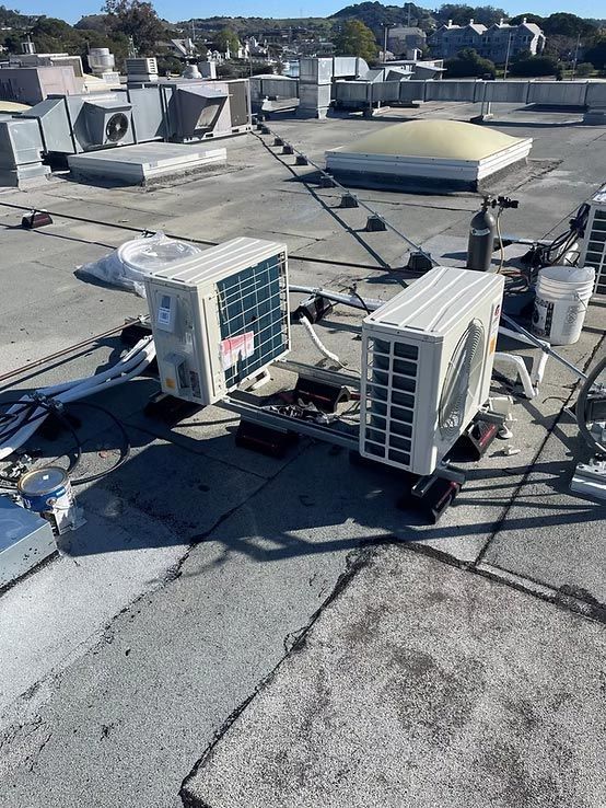 Rooftop with two HVAC units, ventilation ducts, and a dome skylight on a flat, weathered roof.