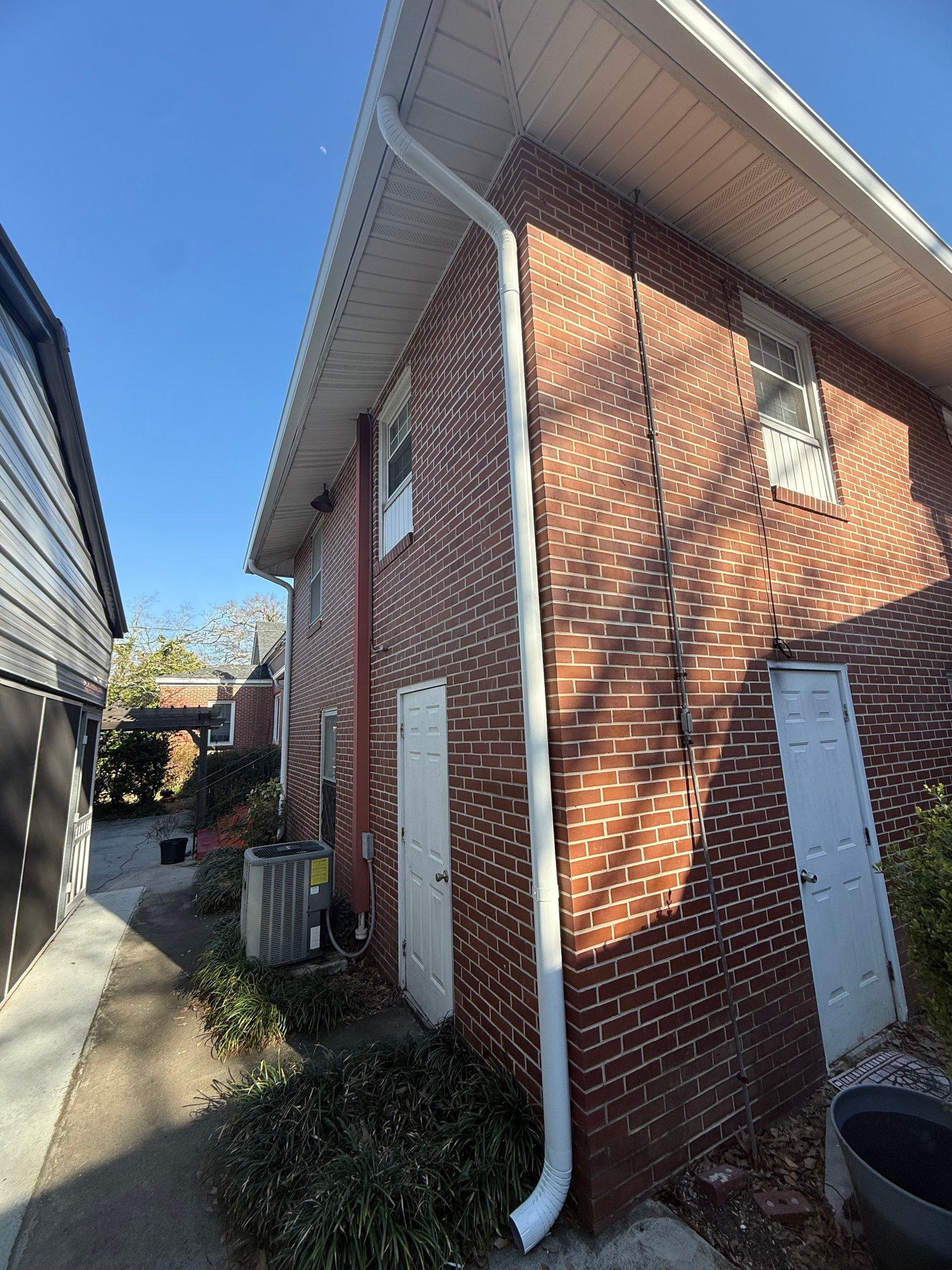 Narrow alley beside a red brick house with white gutters and a blue sky overhead