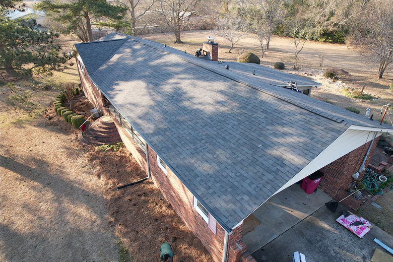 Aerial view of a shingled roof with a ridge vent, a yellow tool box, and a worker near the edge