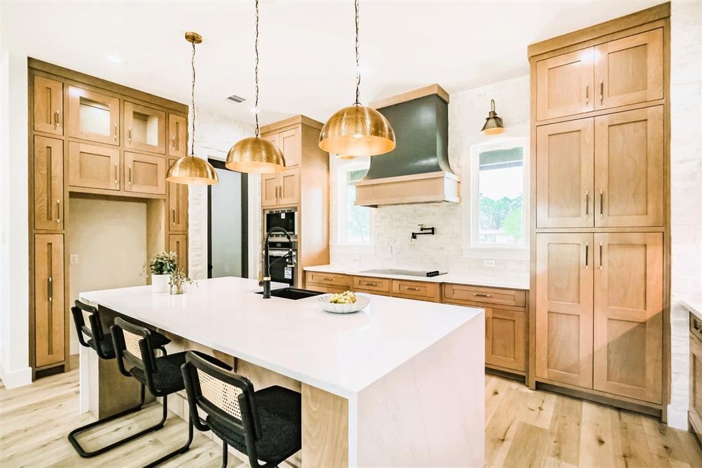 Modern kitchen with wood cabinets, white island, black bar stools, and brass pendant lights