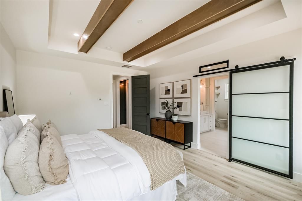 Bright modern bedroom with white bedding, wood ceiling beams, mirrored closet, and black-framed sliding door