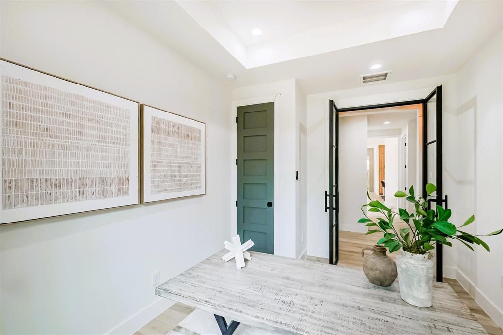 Bright hallway with white walls, framed art, green door, open doorway, and a table with potted plants.