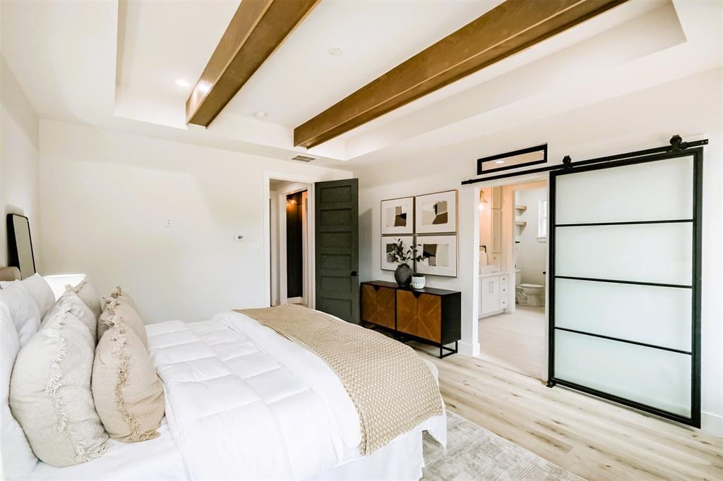 Bright bedroom with white bed, exposed wood beams, and black-framed glass closet doors