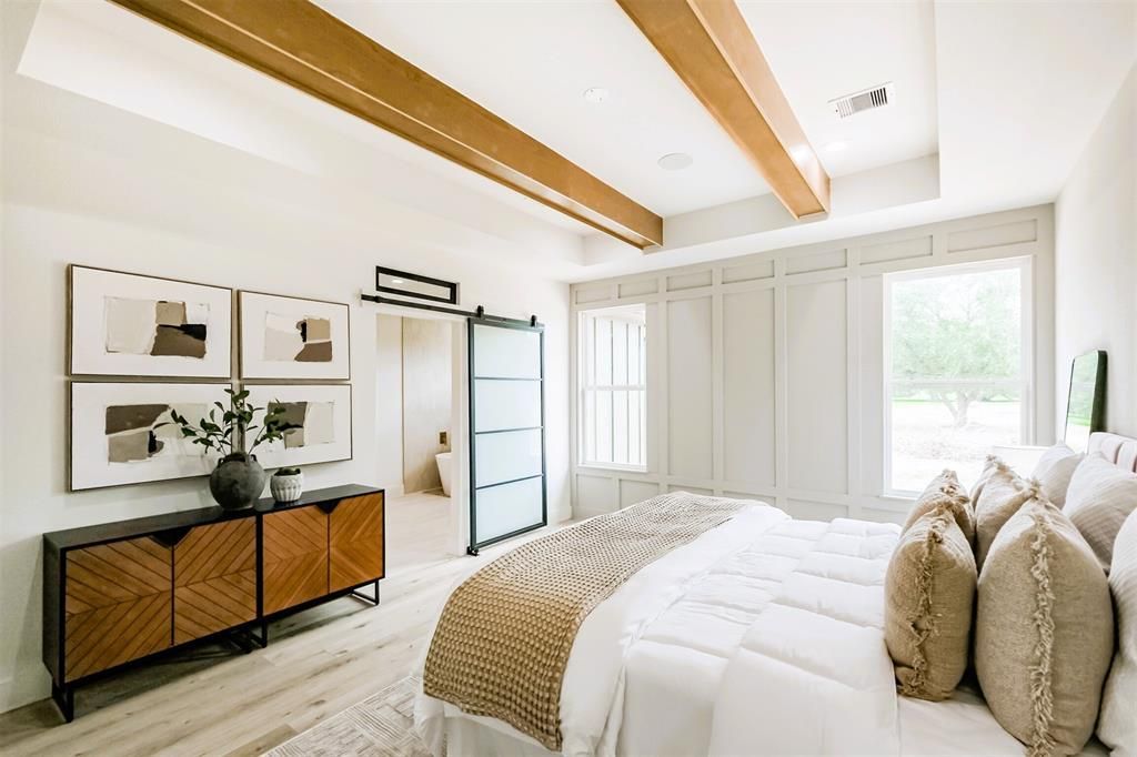 Bright airy bedroom with white bedding, wood ceiling beams, framed art, and sliding glass doors to a balcony