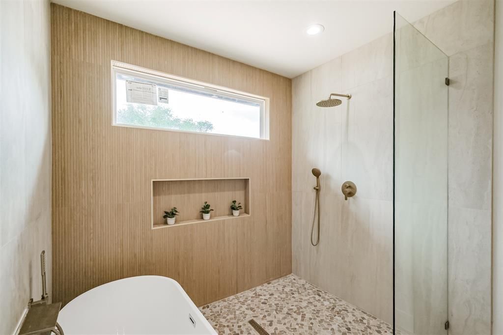 Modern bathroom with wood accent wall, walk-in glass shower, pebble floor, and wall niches