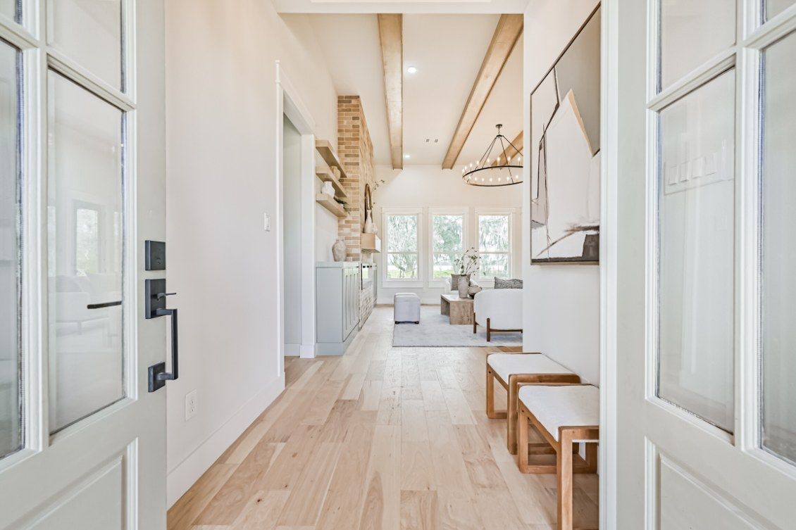 A bright, light-filled entryway with white walls, light wood floors, and two wooden benches leading into a living room.