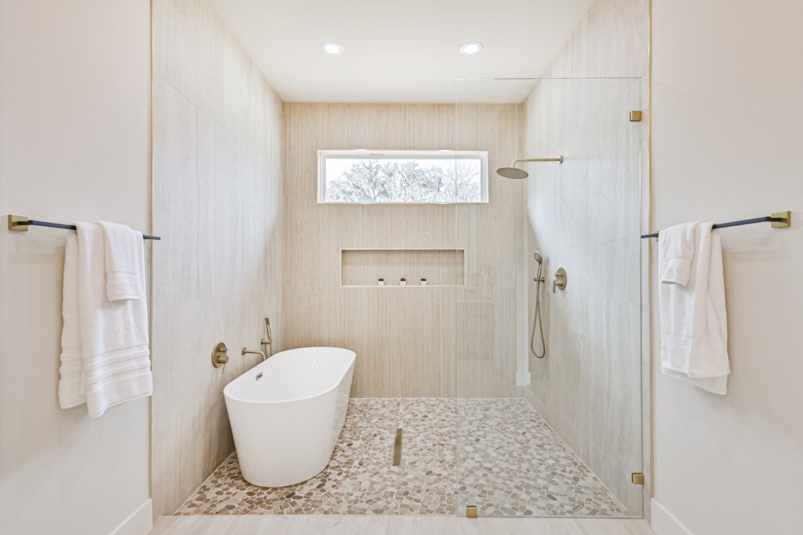 A modern bathroom featuring a white freestanding tub, a walk-in shower with stone tile floors, and brass hardware.