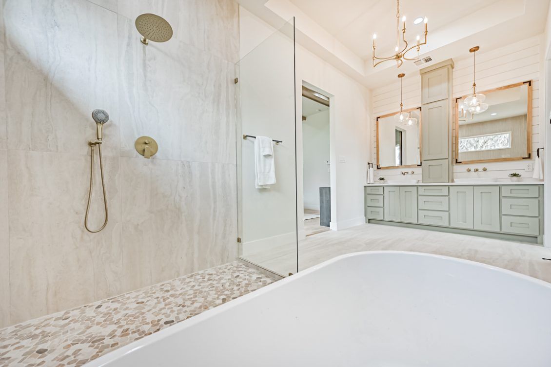 A bright, luxury bathroom features a freestanding tub, a glass-enclosed shower with pebble flooring, and dual vanities.