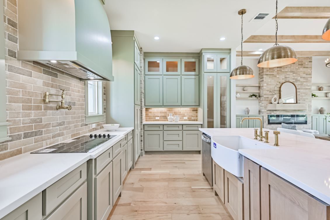A bright, modern kitchen featuring sage green cabinets, light wood flooring, a white island, and pendant lighting.