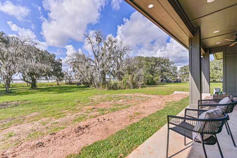 Covered patio overlooking a grassy yard with trees, Spanish moss, and a cloudy blue sky.