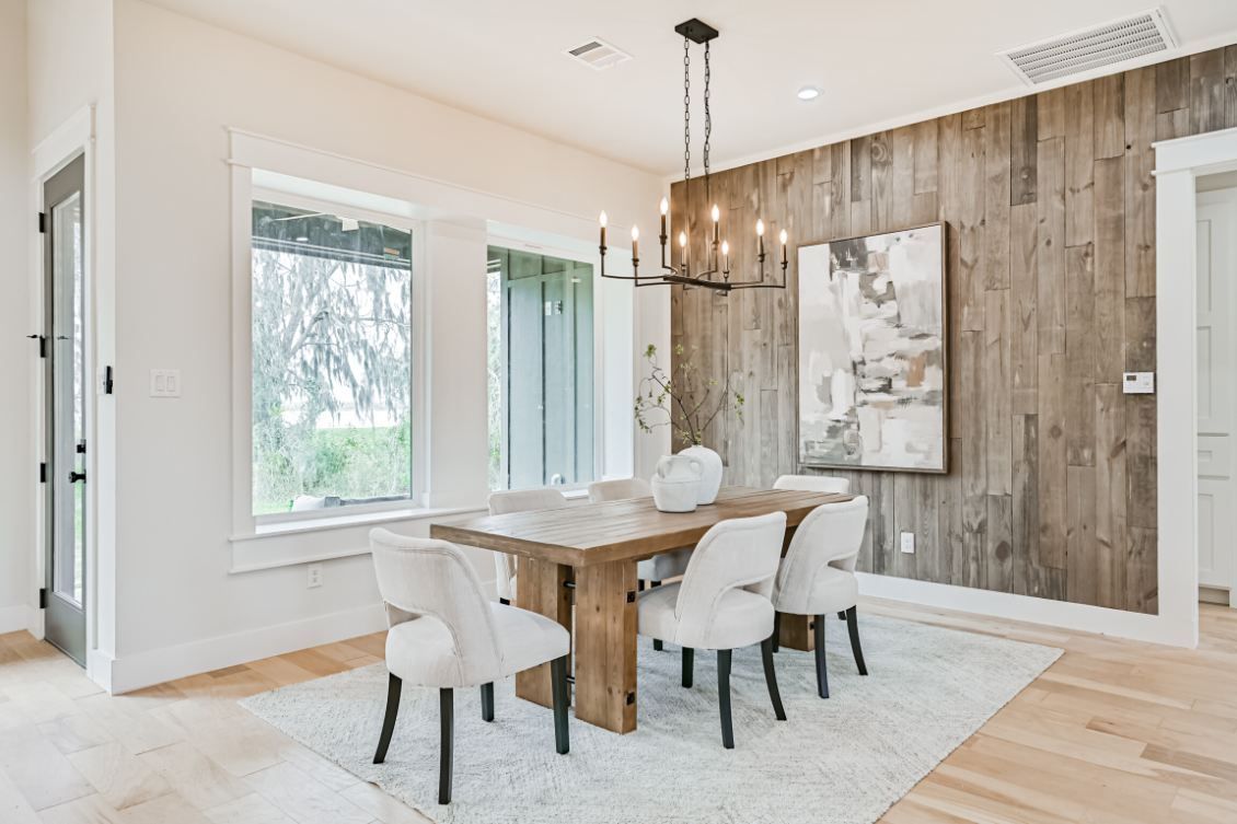 Dining room with a wooden table, four white chairs on a light rug, and an accent wall with rustic wooden planks.