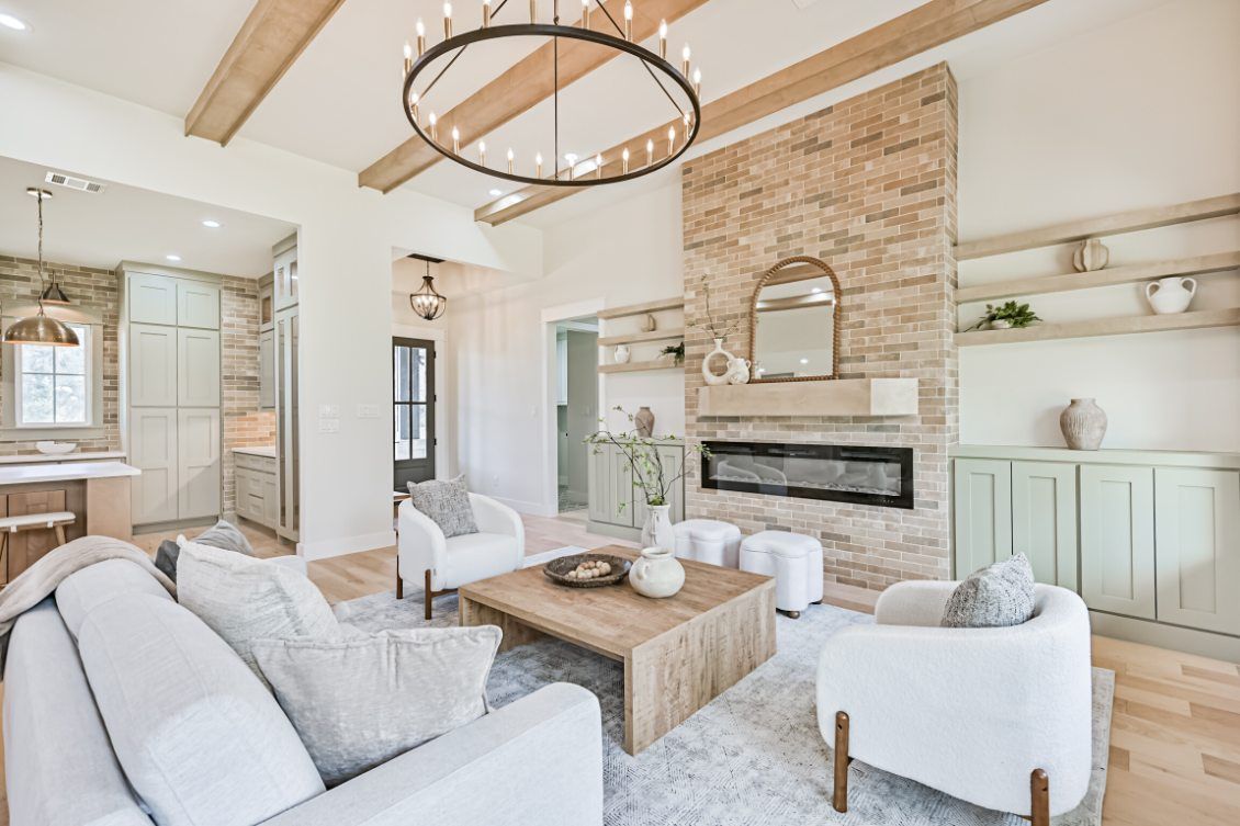 A bright living room with a stone fireplace, beige furniture, wood ceiling beams, and a large circular chandelier.