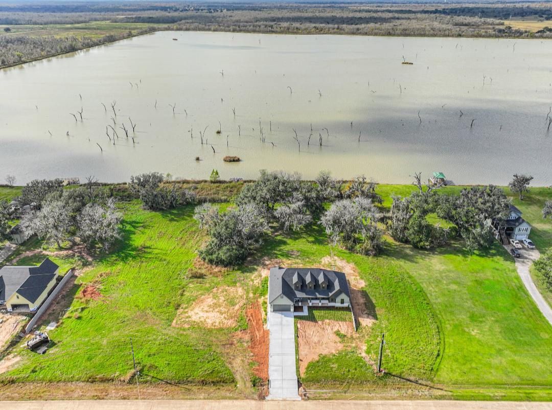 Aerial view of a suburban home under construction beside a large lake with scattered trees in a rural setting.