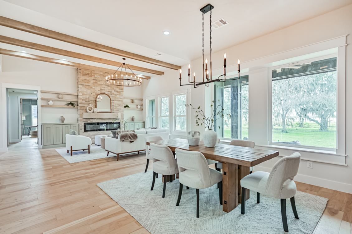 A bright, modern open-plan dining and living area with a wood table, cream chairs, stone fireplace, and light wood floors.