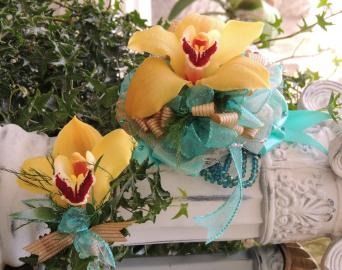 Yellow orchid floral arrangement with teal ribbon in a decorative white vase