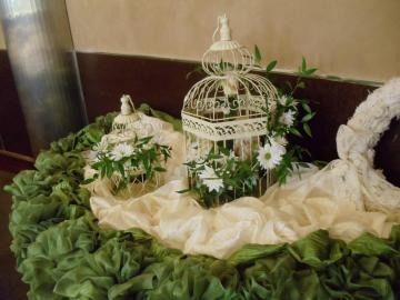 White decorative birdcages with flowers on ruffled cream and green fabric display.