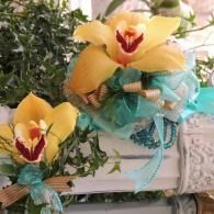 Two yellow orchid floral arrangements with teal ribbons on a decorative white shelf
