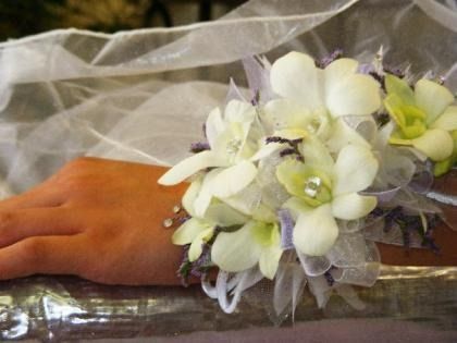 White and pale green flower wrist corsage on a hand resting on a table