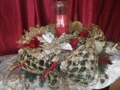 Decorative holiday centerpiece with gold mesh, red accents, and white flowers on a red draped background