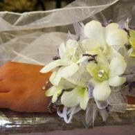 White flower corsage with pale purple accents on a wrist beside a brown surface