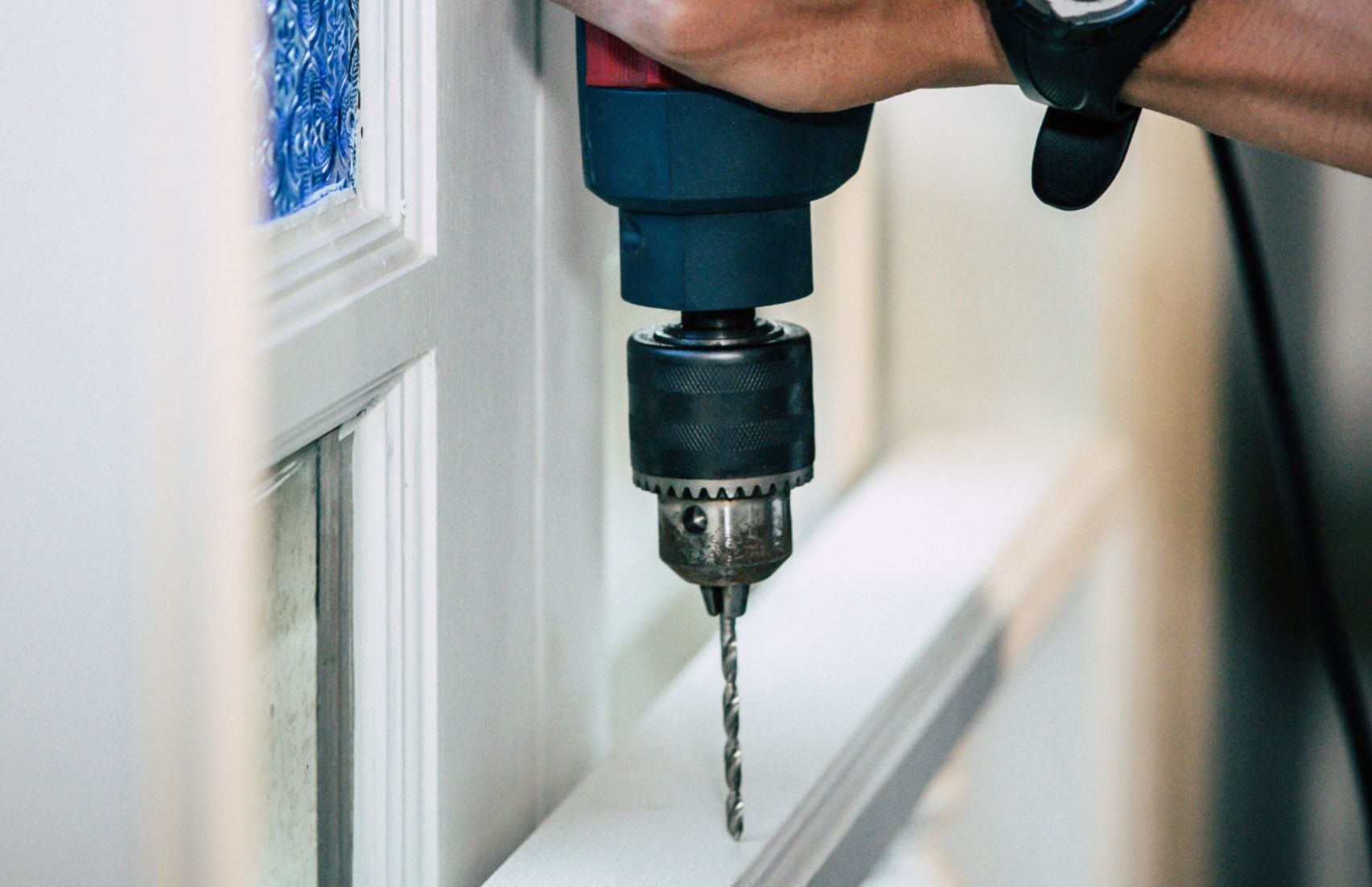 Person using a power drill to make a hole in white trim.