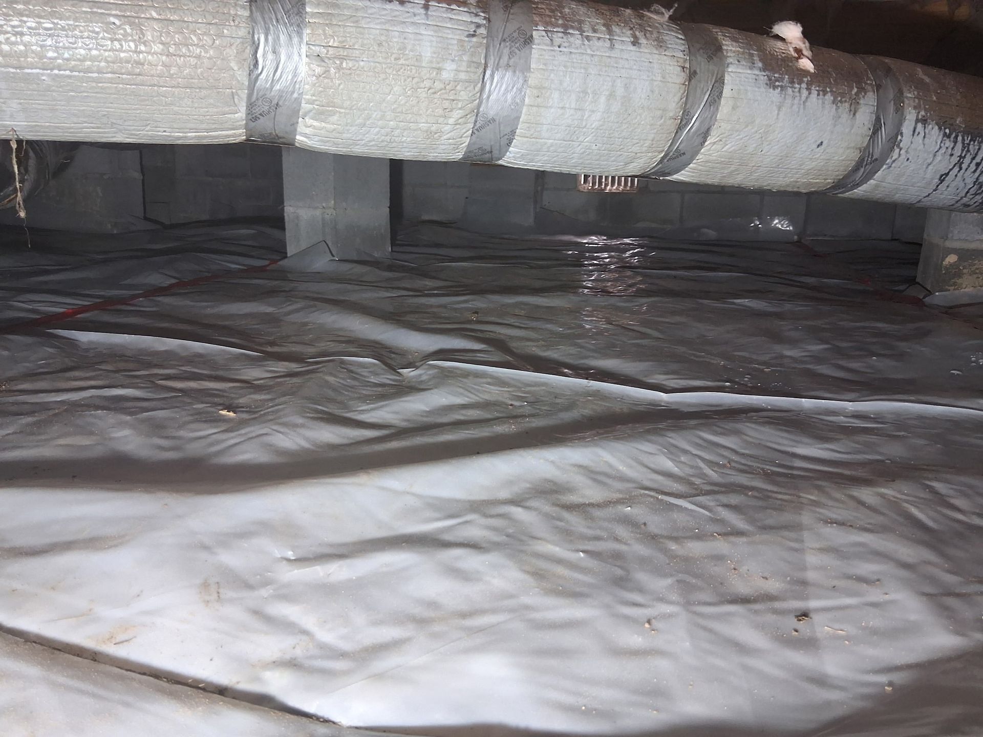 Insulated ductwork above a white vapor barrier in a crawlspace or attic area