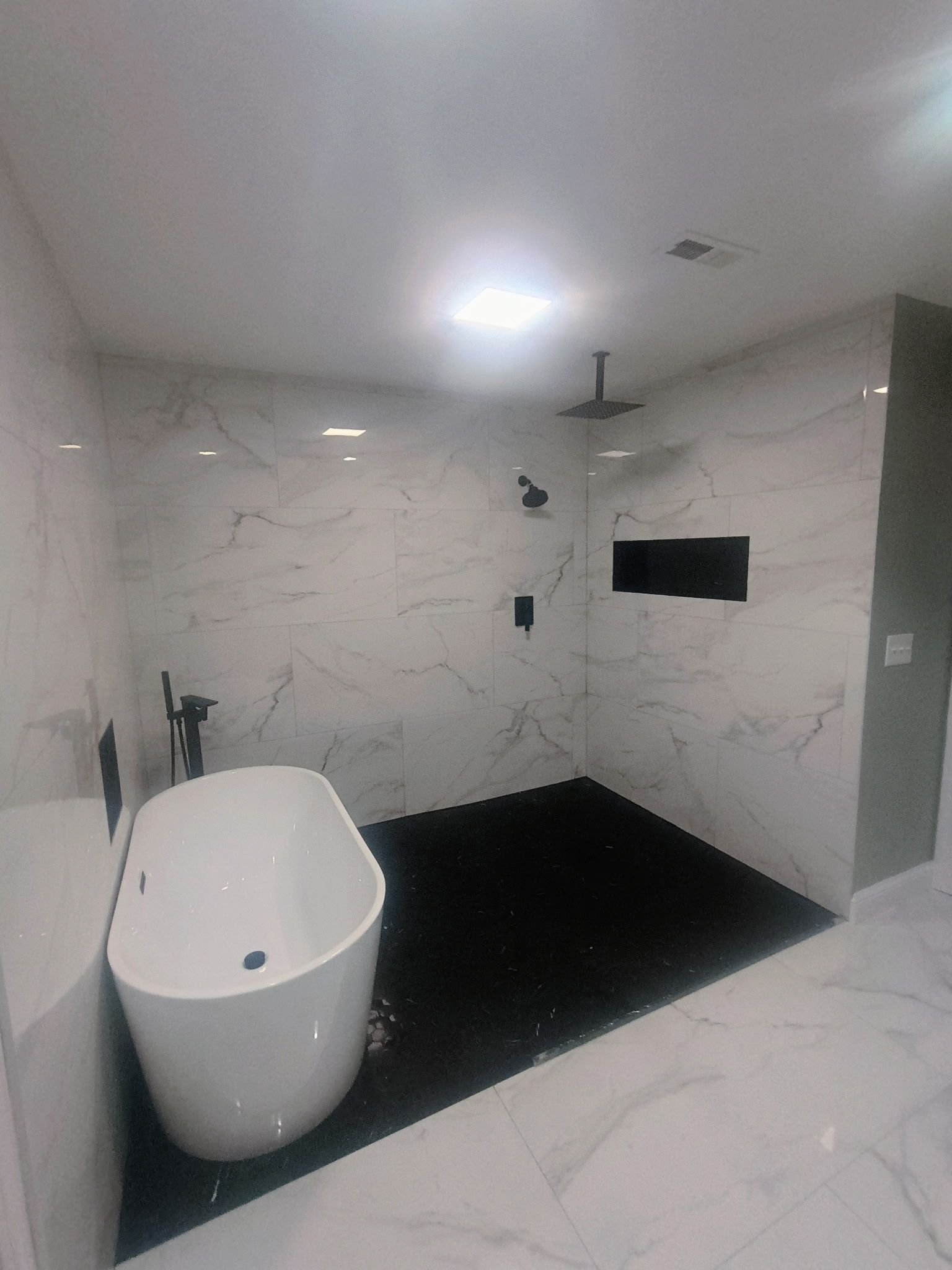 Modern white marble bathroom with a freestanding tub, walk-in shower, and black floor tiles.