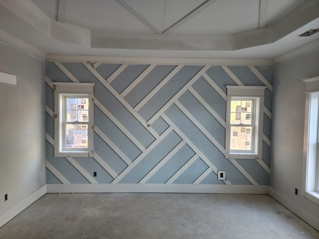 Empty room with gray herringbone accent wall and two windows, unfinished carpeted floor.