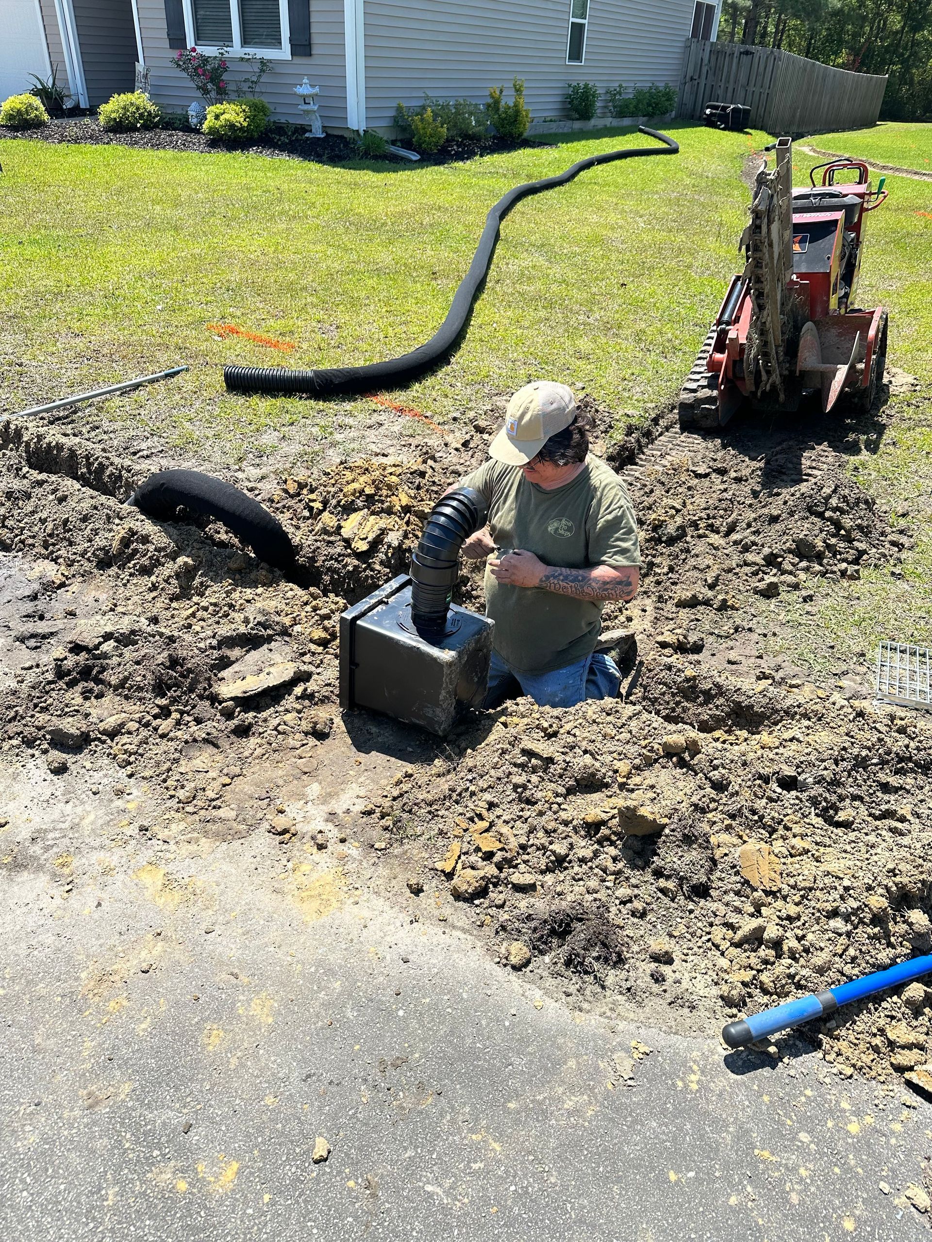 Worker installing utility pipe in muddy trench beside house and excavator