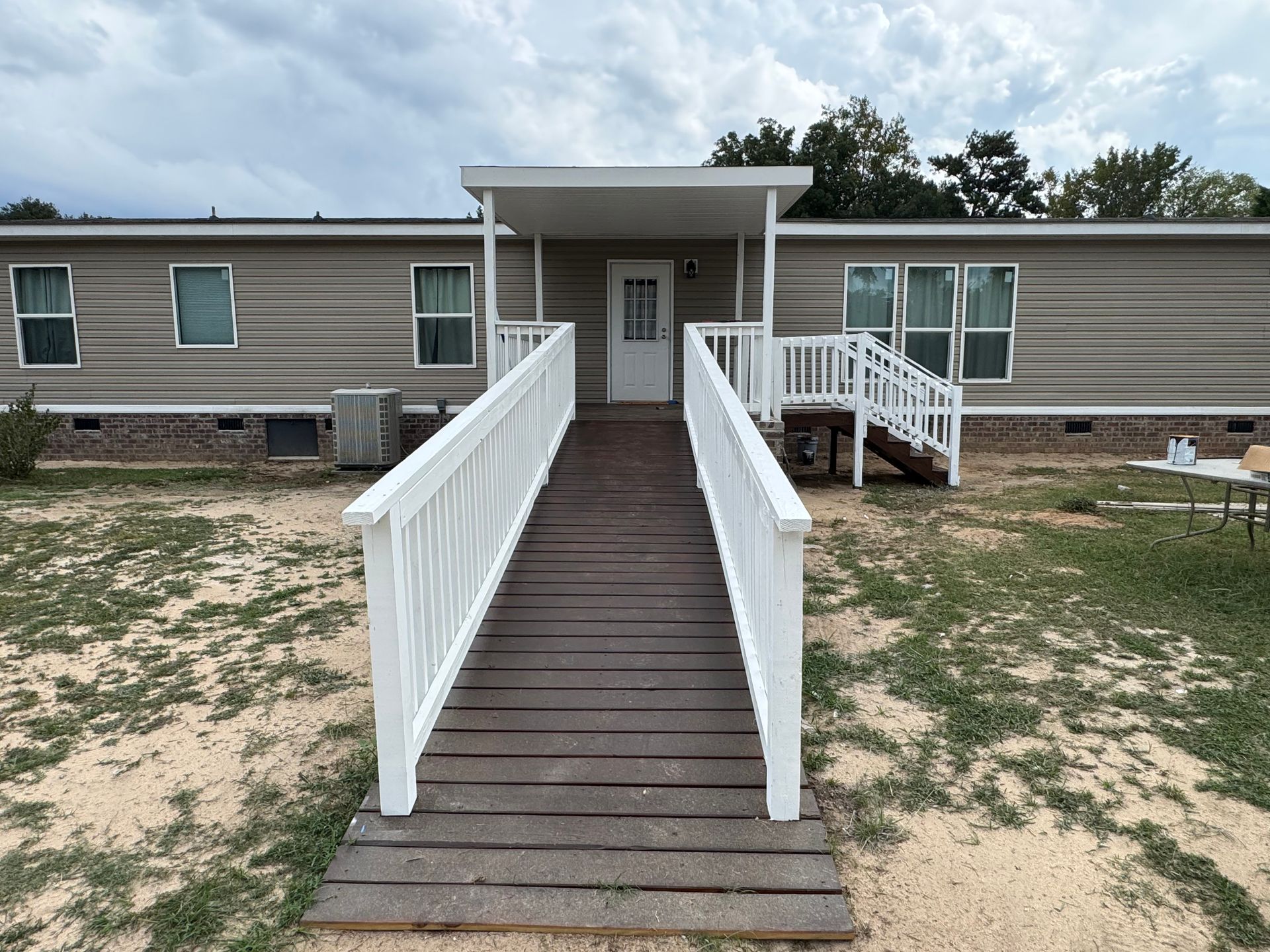 Accessible ramp leading to a beige mobile home with a front door and white railings