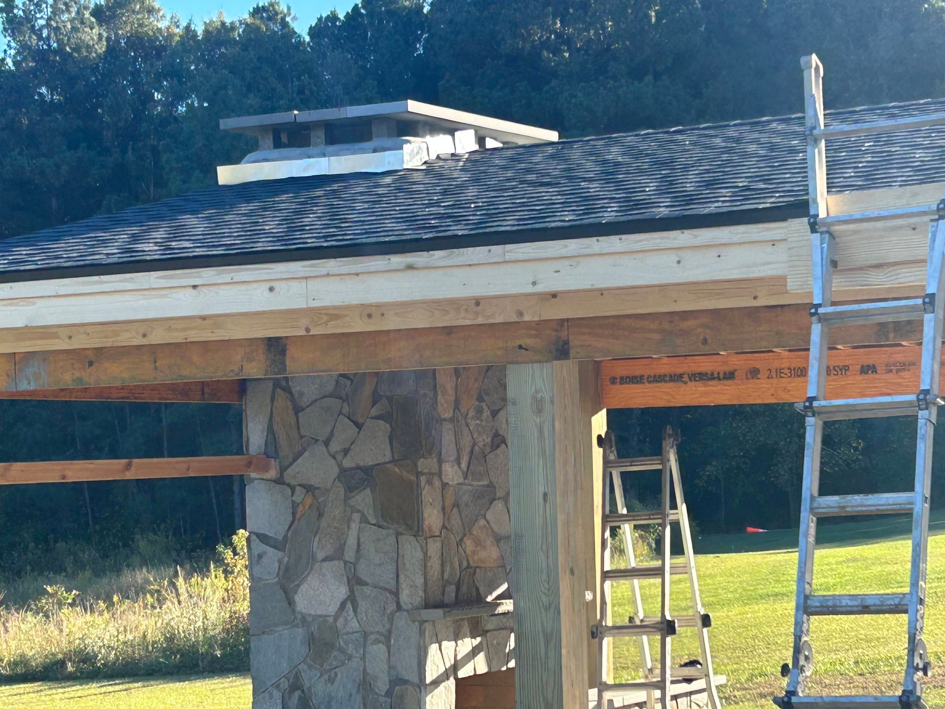 Stone pillar supporting a roof under construction, with ladders and exposed wood beams in a sunny outdoor setting