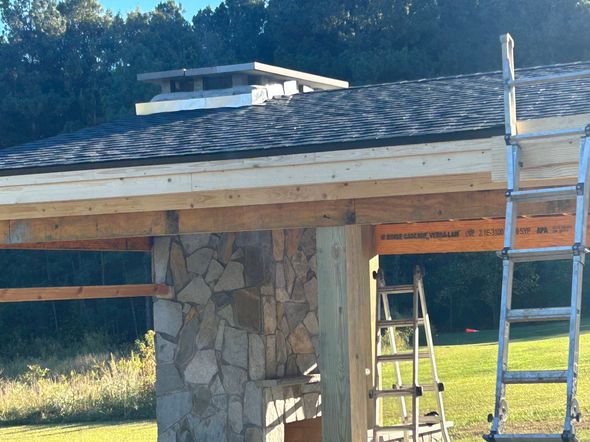 Stone pillar supporting a roof under construction, with ladders and exposed wood beams in a sunny outdoor setting