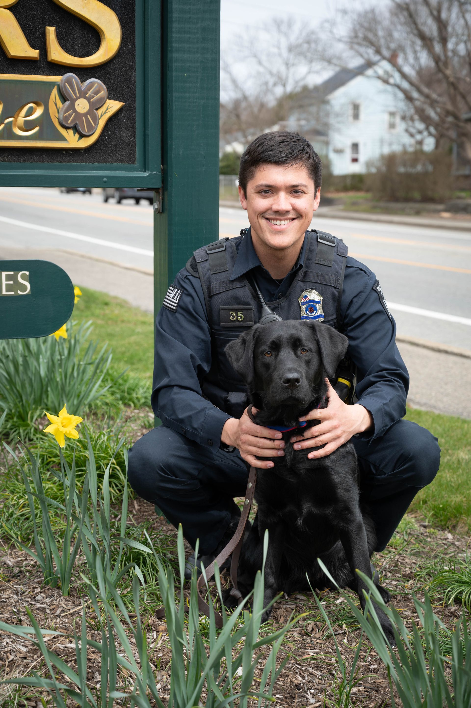 A police officer is posing for a picture with a black dog.