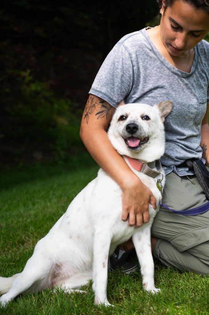 A woman is kneeling down next to a white dog in the grass.